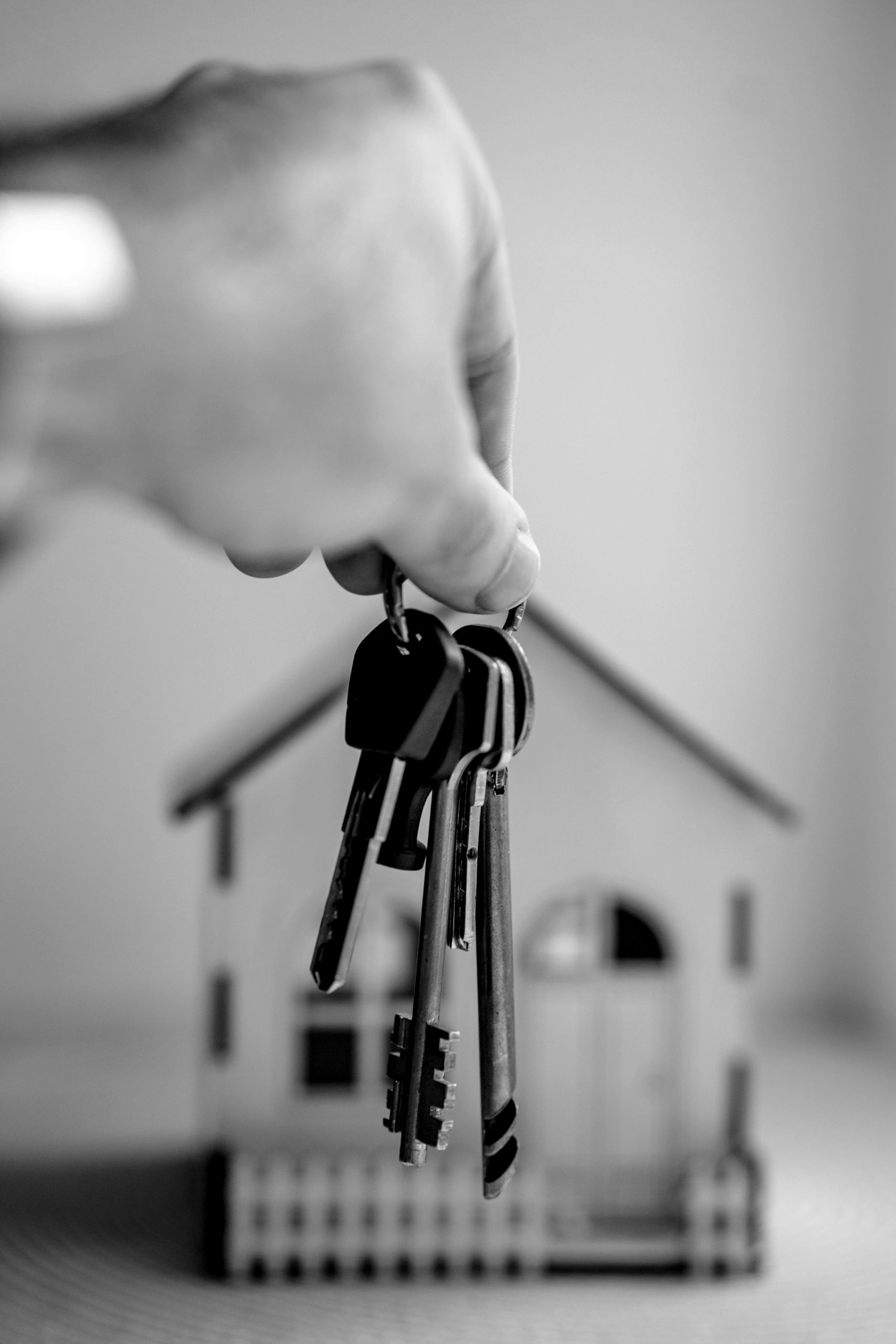 Hand reicht Schluessel in Richtung eines Miniatur-Hauses